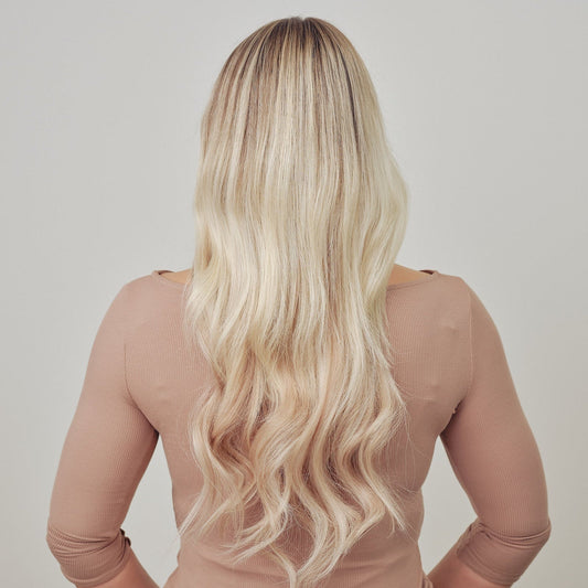 Person with long blonde hair wearing a sheer beige top against a plain background