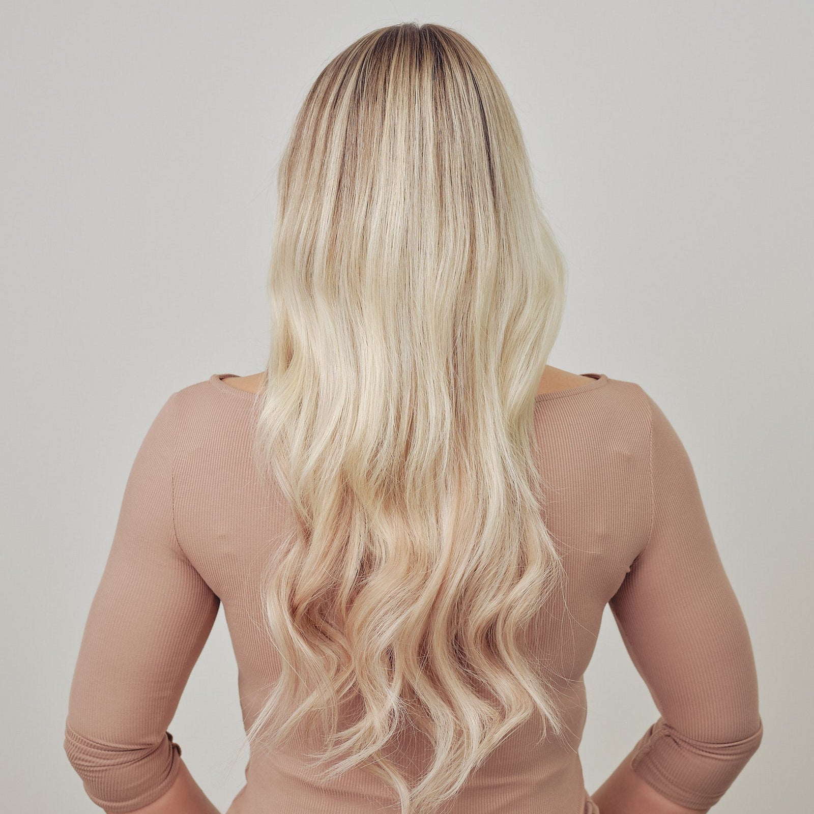 Person with long blonde hair wearing a sheer beige top against a plain background