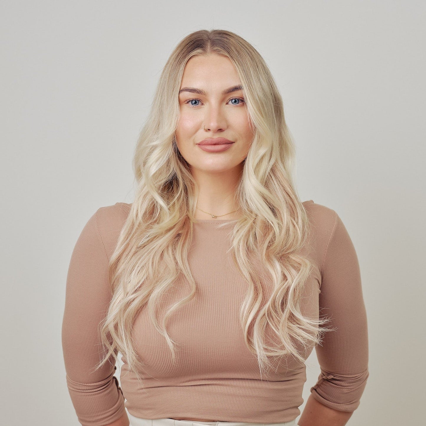 Woman with long blonde hair clip in hair extensions against a plain background
