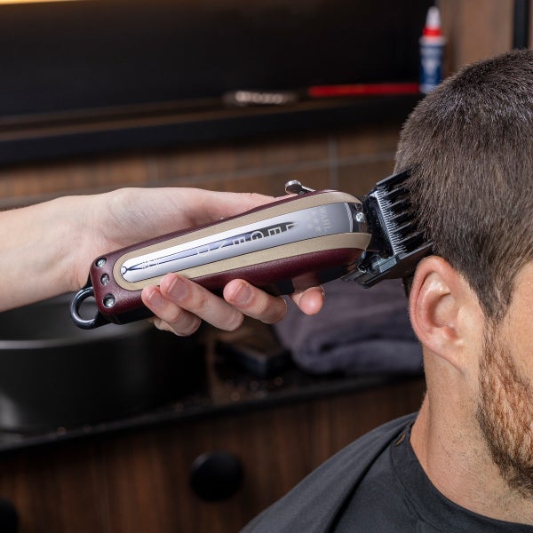 Person using a hair clipper on another person's head in a barbershop setting.