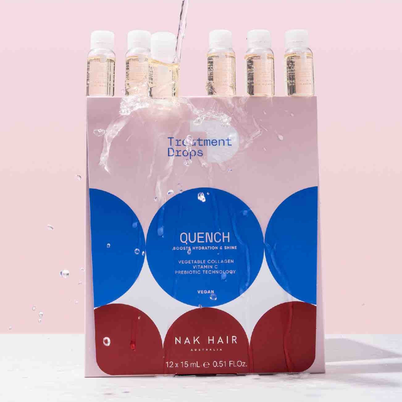 A pink, white, and blue box of NAK HAIR Quench Treatment Drops with water being poured over the top, showing the clear bottles and liquid splash against a solid pink background.