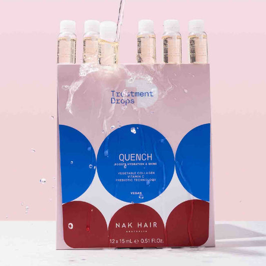 A pink, white, and blue box of NAK HAIR Quench Treatment Drops with water being poured over the top, showing the clear bottles and liquid splash against a solid pink background.