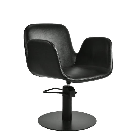 A modern black salon chair with a curved, sculptural seat and backrest, mounted on a black hydraulic swivel base with a circular footrest, shown against a plain white background.